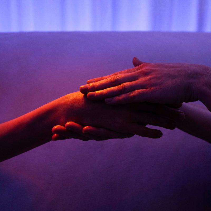 Two hands reaching towards each other with a purple filter.