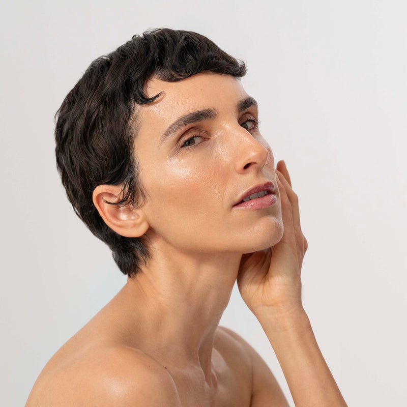 Person with short hair touching their face against a plain background
