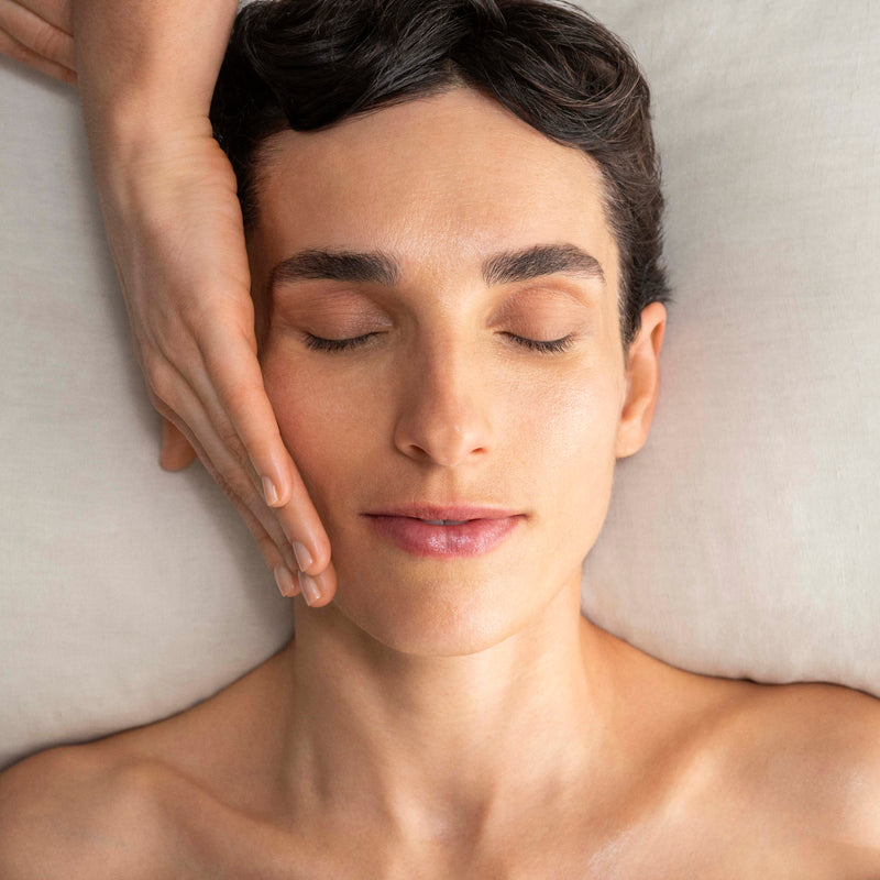 Woman receiving a facial massage with a hand on his face, lying on a neutral background