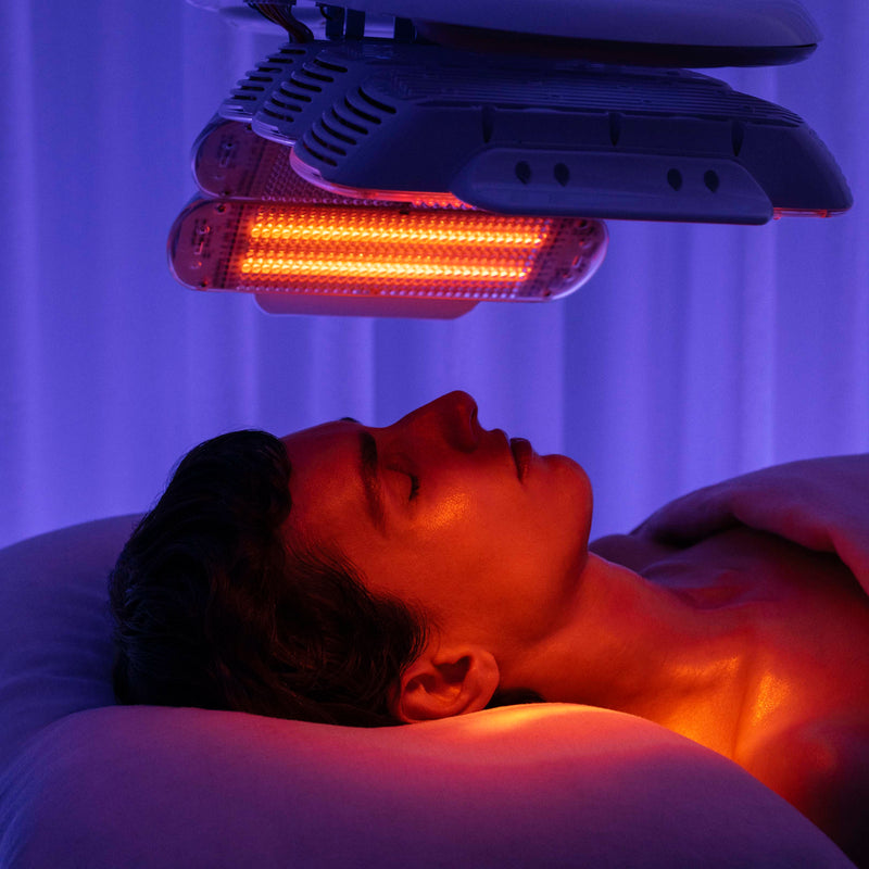 Person receiving red light therapy under a device with a purple background
