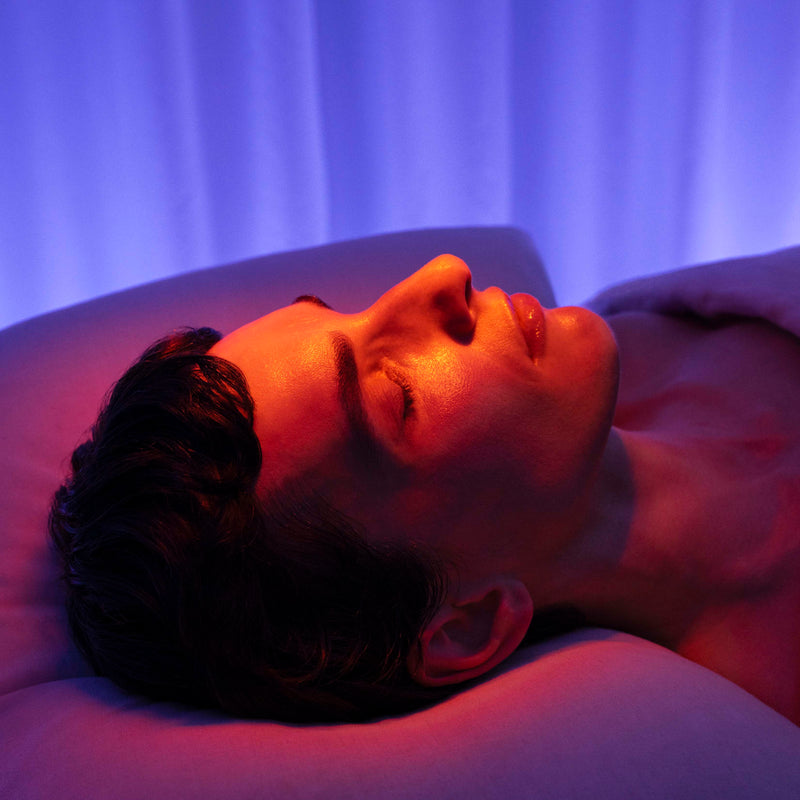 Person lying down with a purple light therapy device on their face