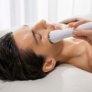 Woman receiving a facial treatment with a handheld device against a white curtain background
