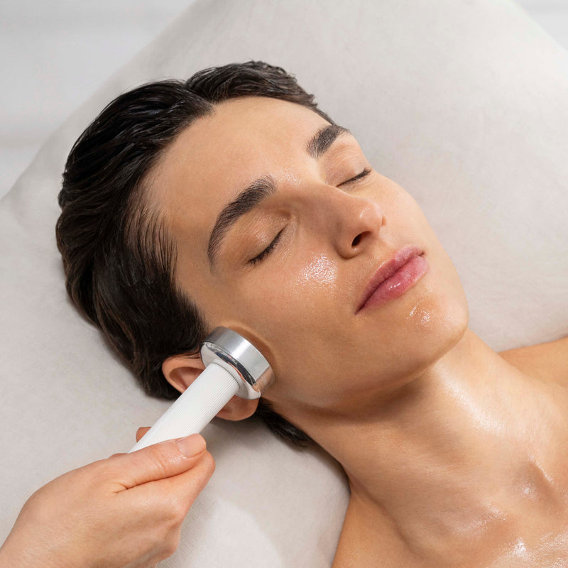 Person receiving facial treatment with a device on a white background