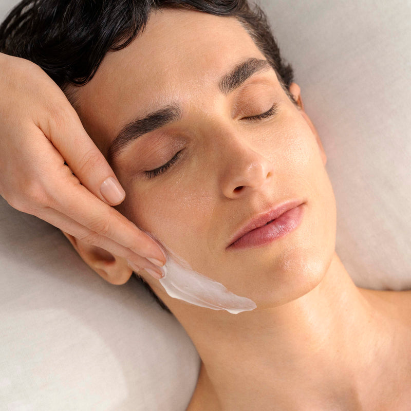 Woman receiving a facial treatment with a hand applying cream to her face.