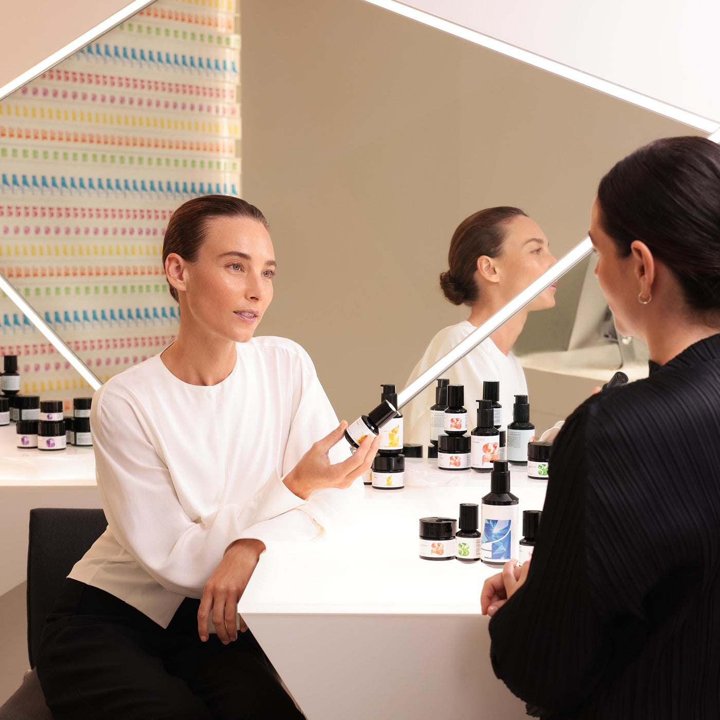 Two women in a consultation setting with skincare products on a table.