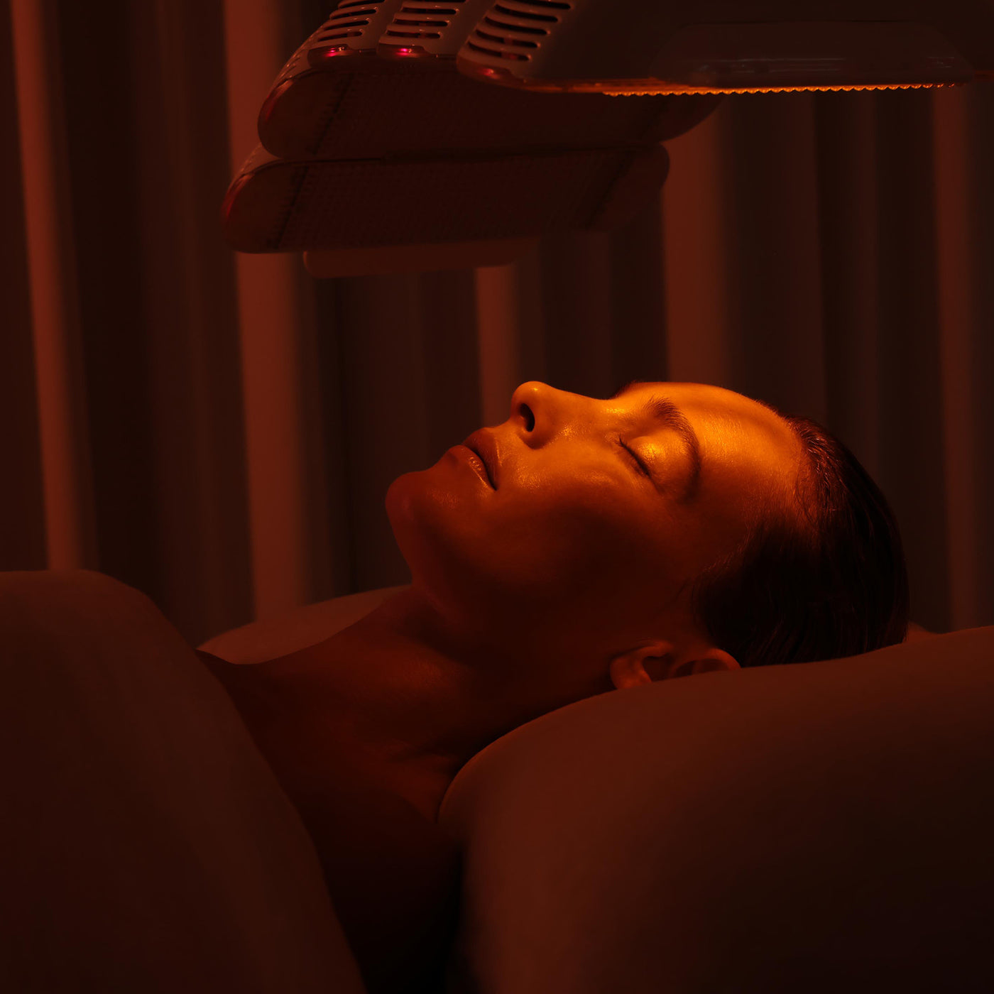 Person receiving a red light therapy treatment under a lamp.