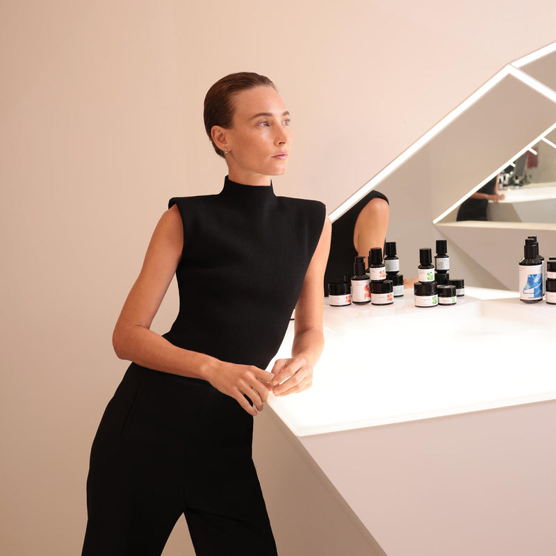 Woman in a black outfit standing in front of a counter with skincare products.