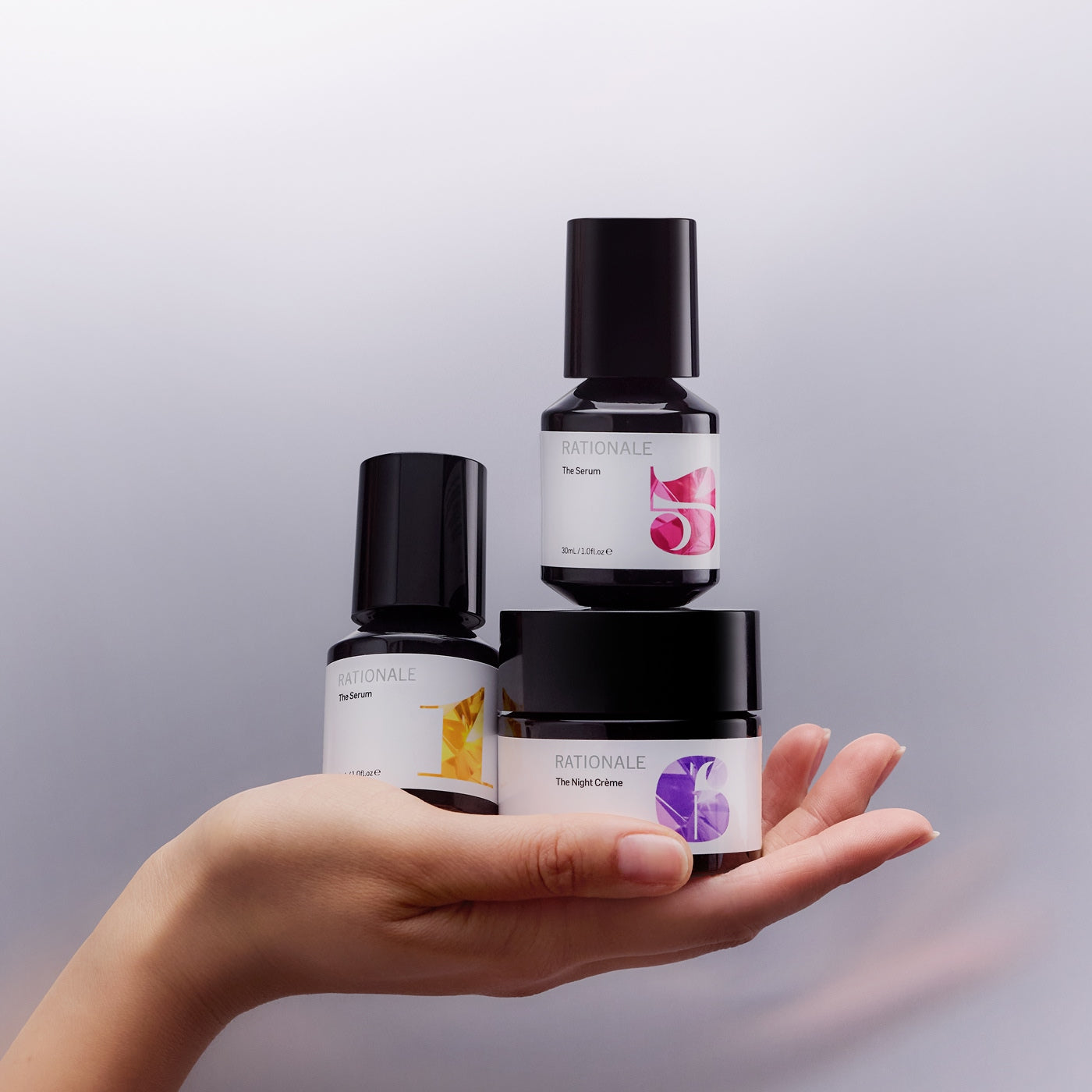 Hand holding three skincare product bottles with visible labels against a light gray background
