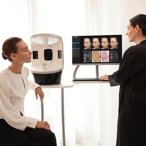 Person using a laptop with facial recognition software on a screen, next to a person wearing a helmet-like device.