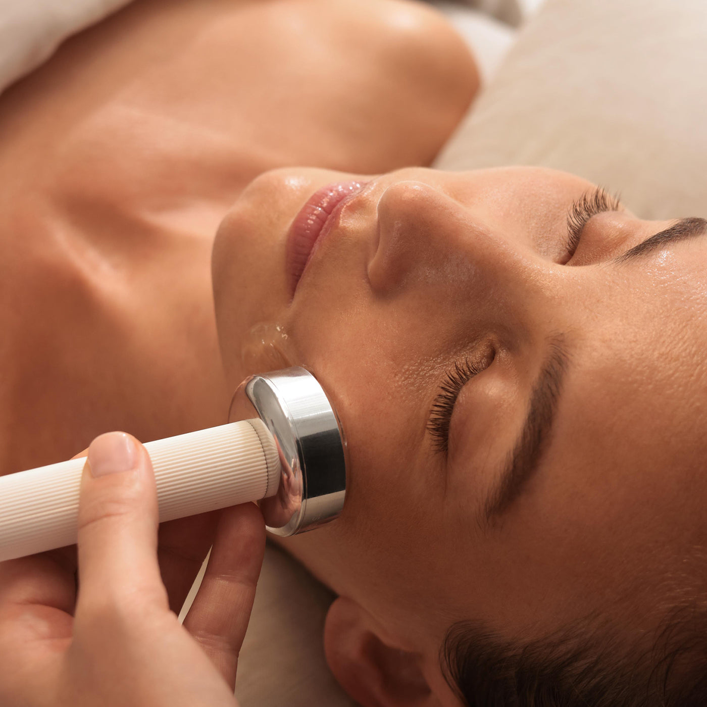 Woman receiving a facial treatment with a handheld device.